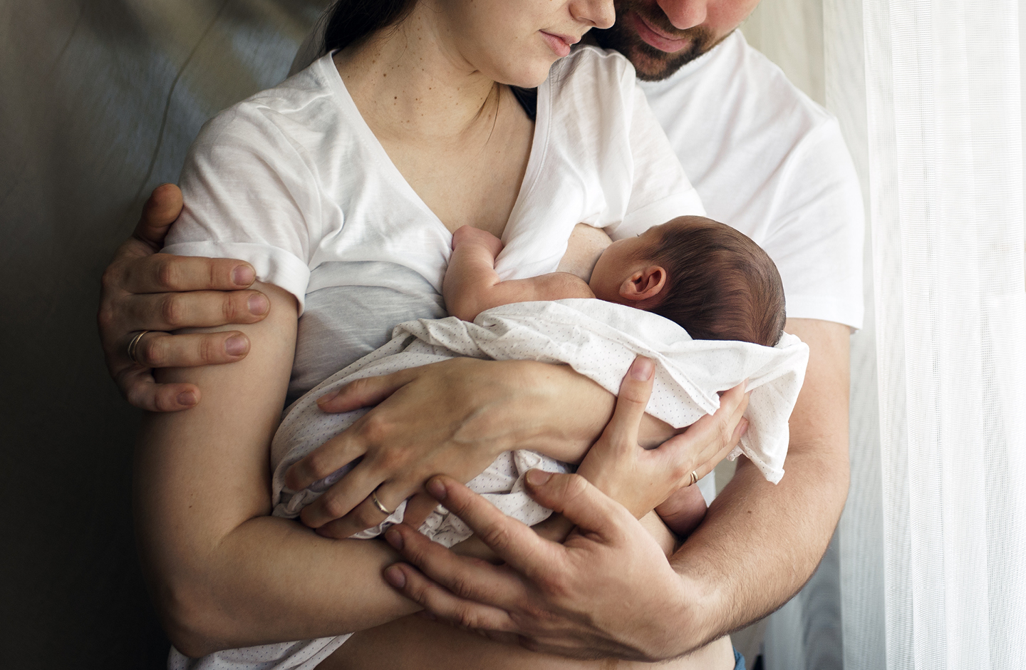 Junger Vater legt zärtlich seine Arme um stillende Mutter , die ihr Baby auf dem Arm hält  