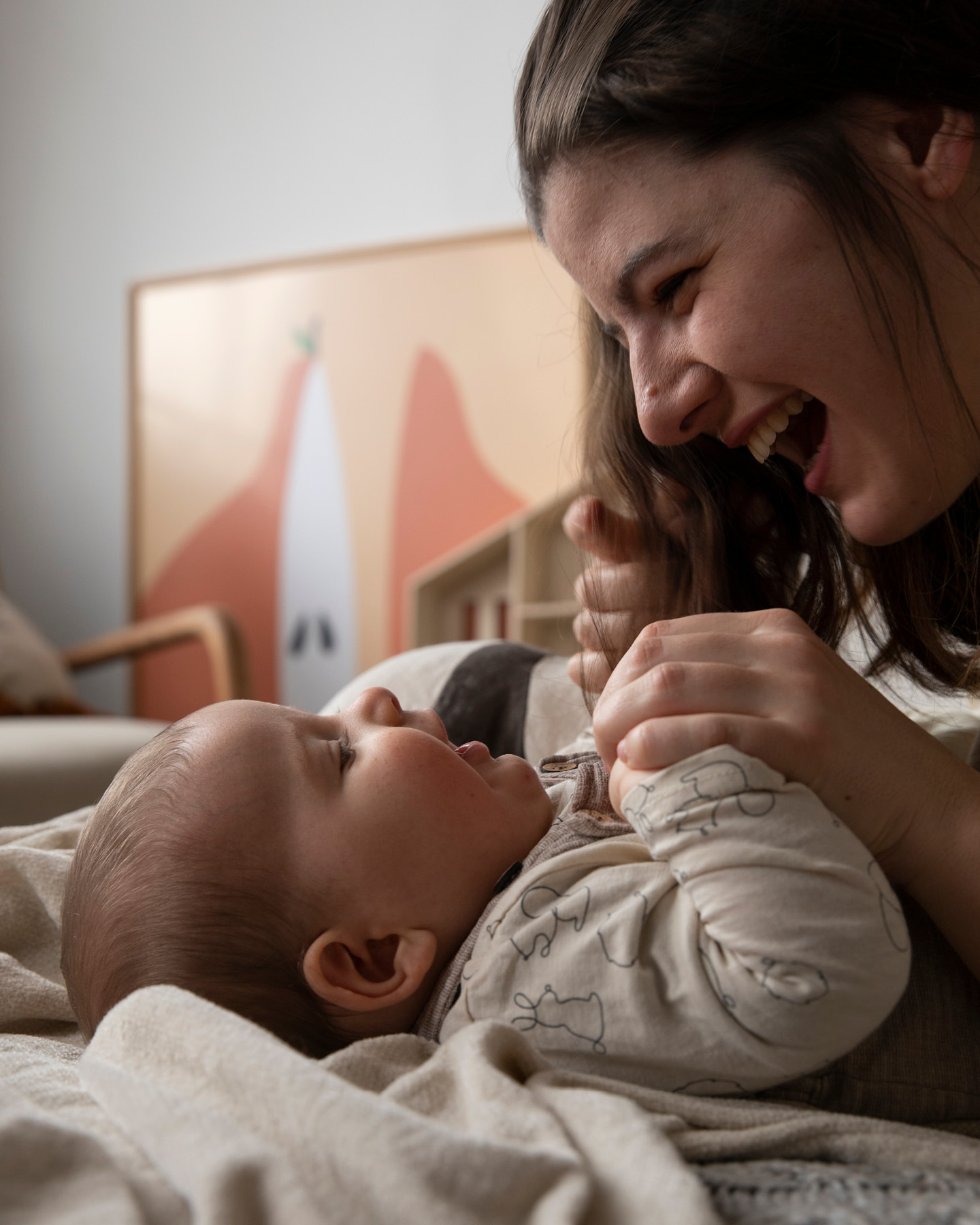 Mutter spielt lachend mit ihrem Baby im Wohnzimmer