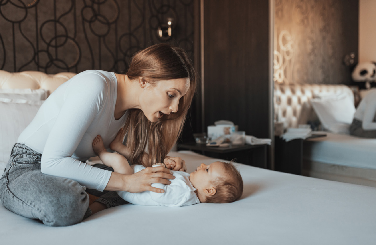 Eine Mutter kniet auf einem Bett und singt ihrem vor ihr liegenden Baby etwas vor