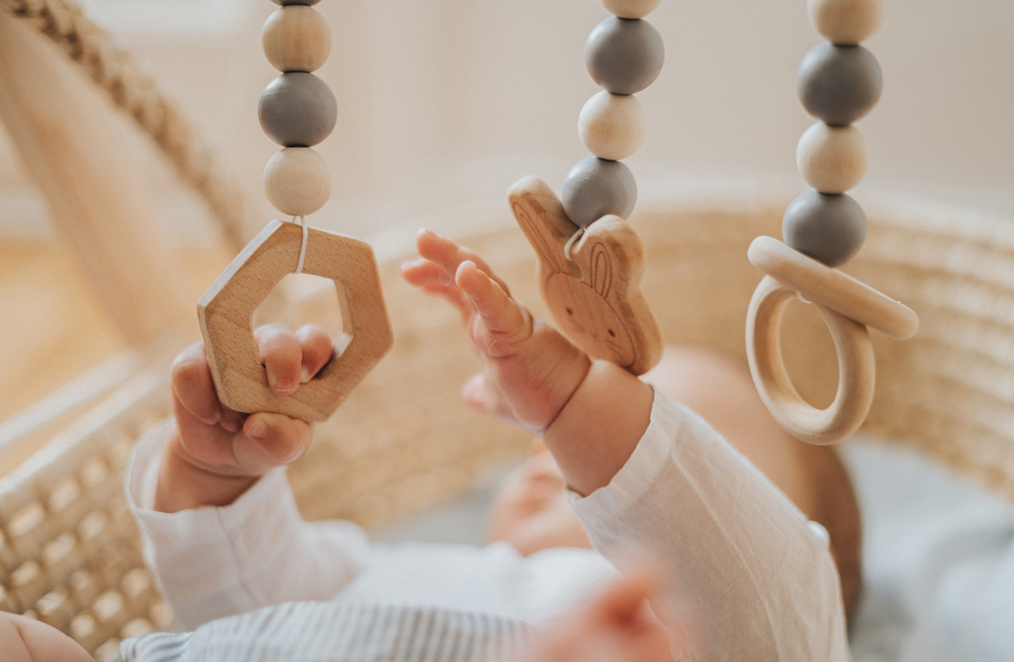 Baby im Körbchen spielt mit nachhaltigen Holz Spielebogen.