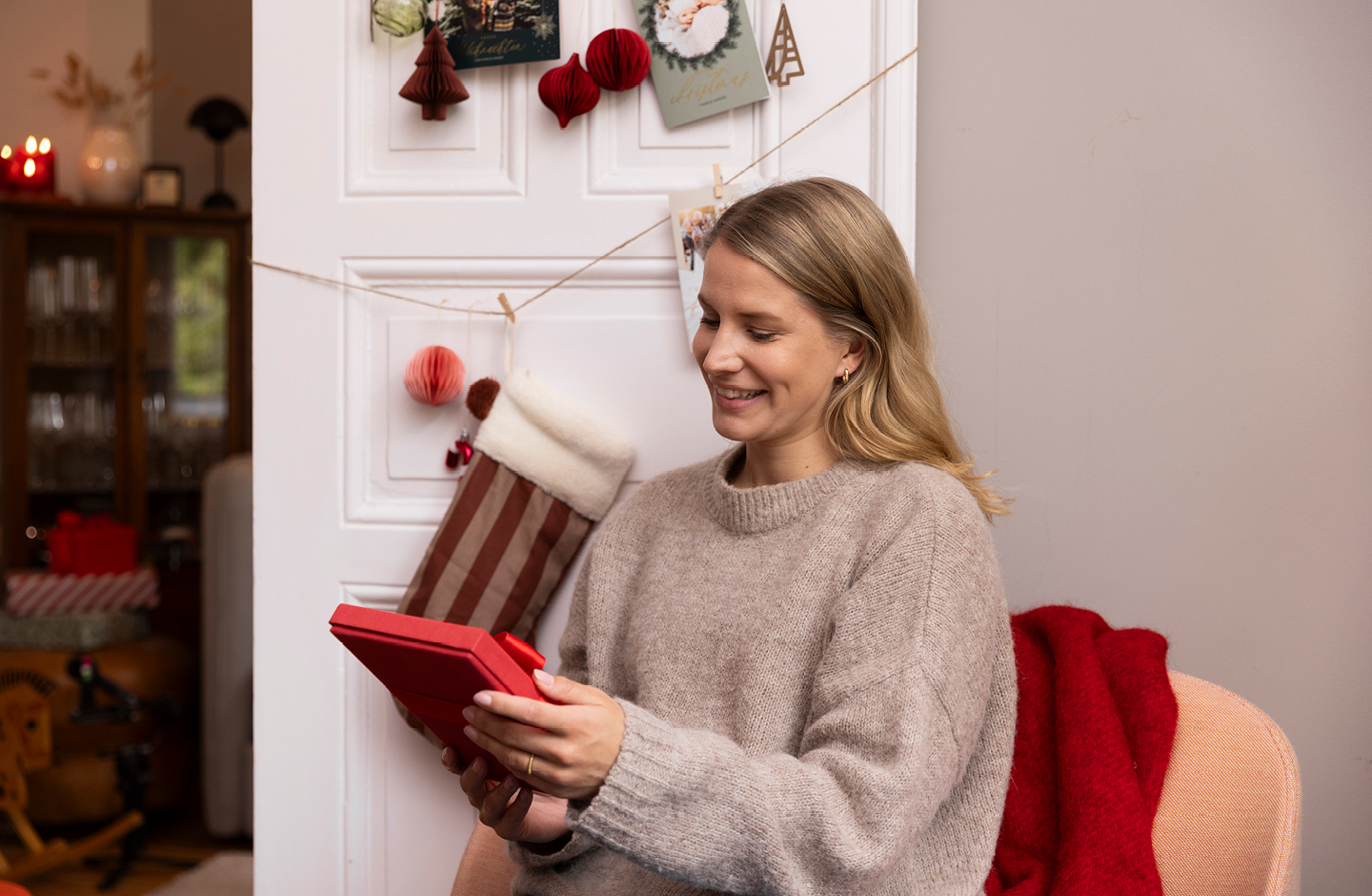 Junge Frau, im Sessel sitzend, hält ein Weihnachtsgeschenk in der Hand