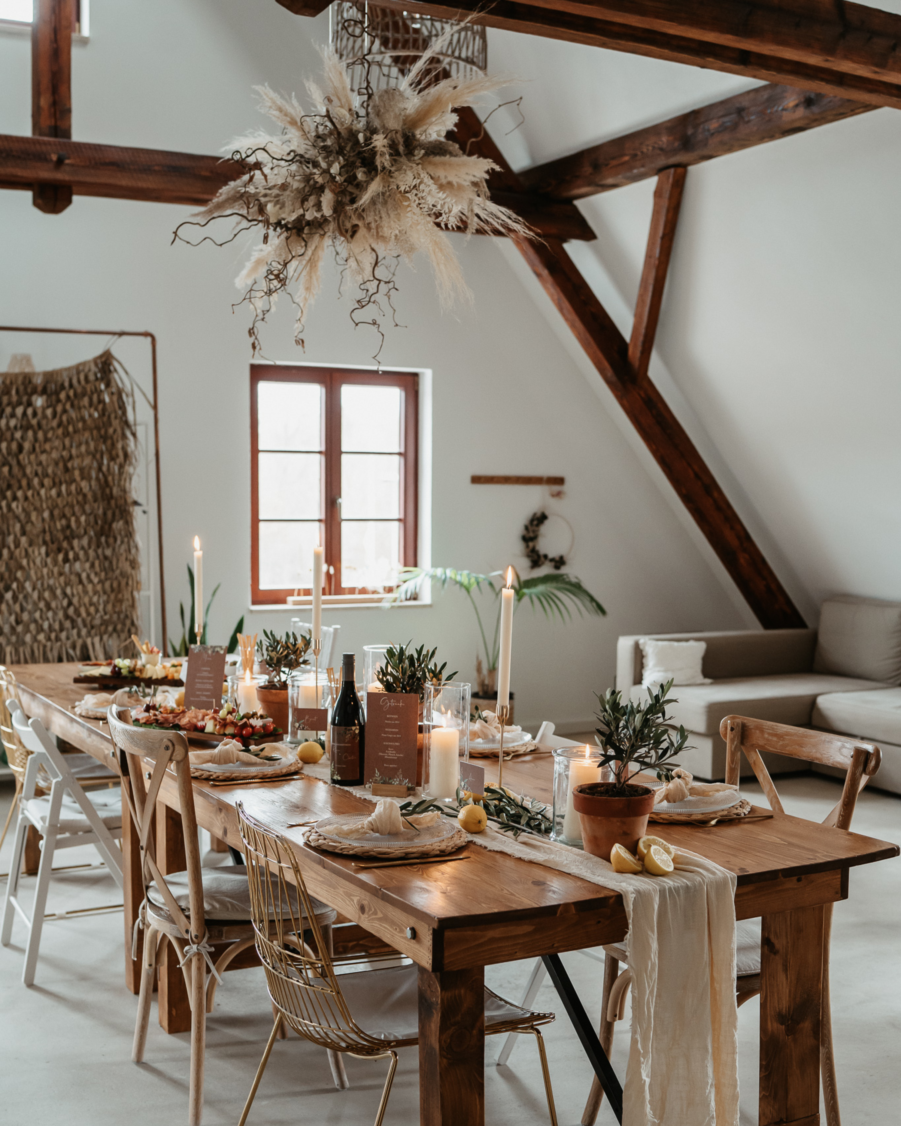 Windlichtern und Olivenzweigen verleihen dem Hochzeitstisch einen rustikalen Look. An der Decke hängt ein üppiges Blumenarrangement aus Pampasgras und Trockenblumen.