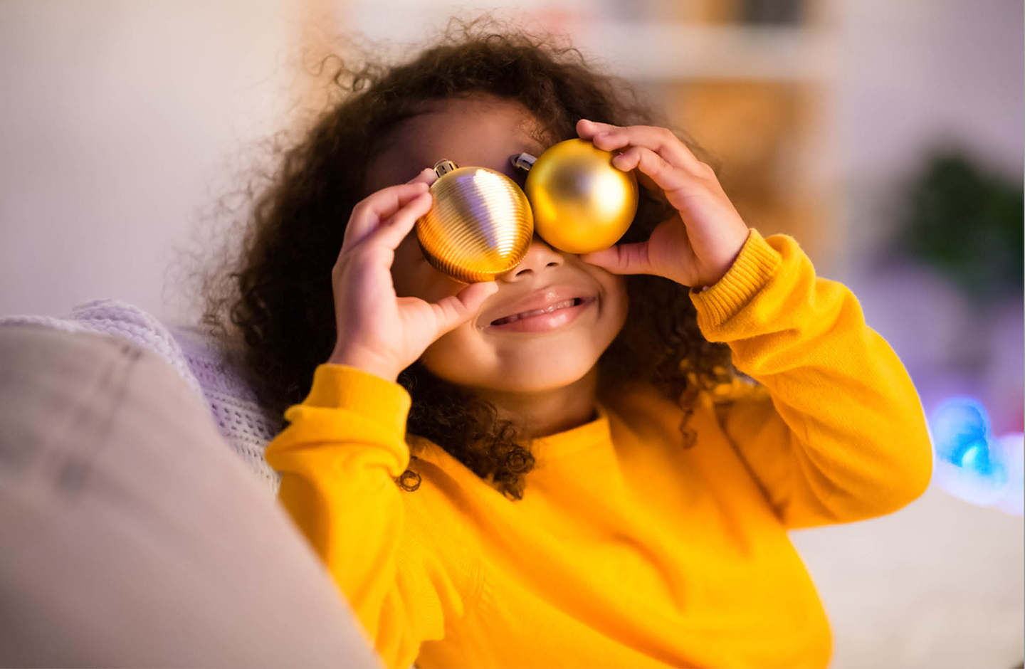 Kleines Mädchen hält sich zwei Weihnachtskugeln vor die Augen. 