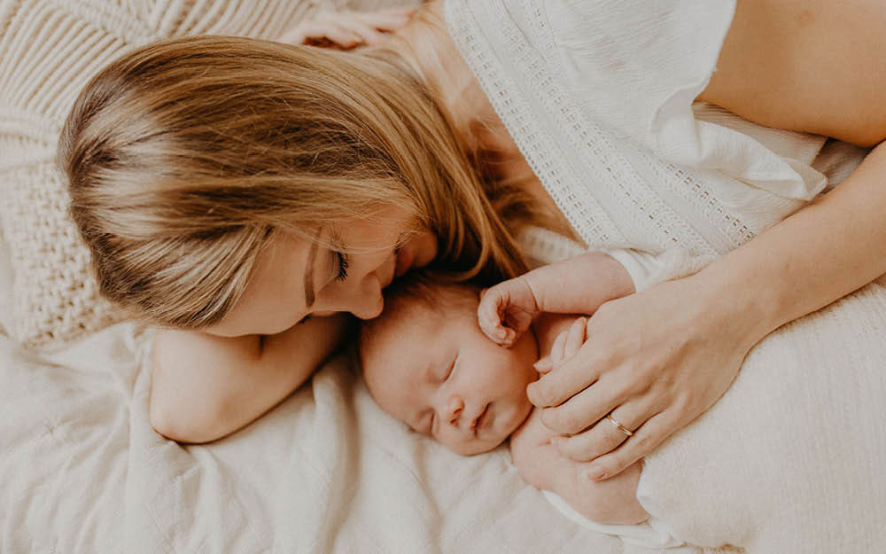 Mama kuschelt mit ihrem schlafenden Baby im Bett