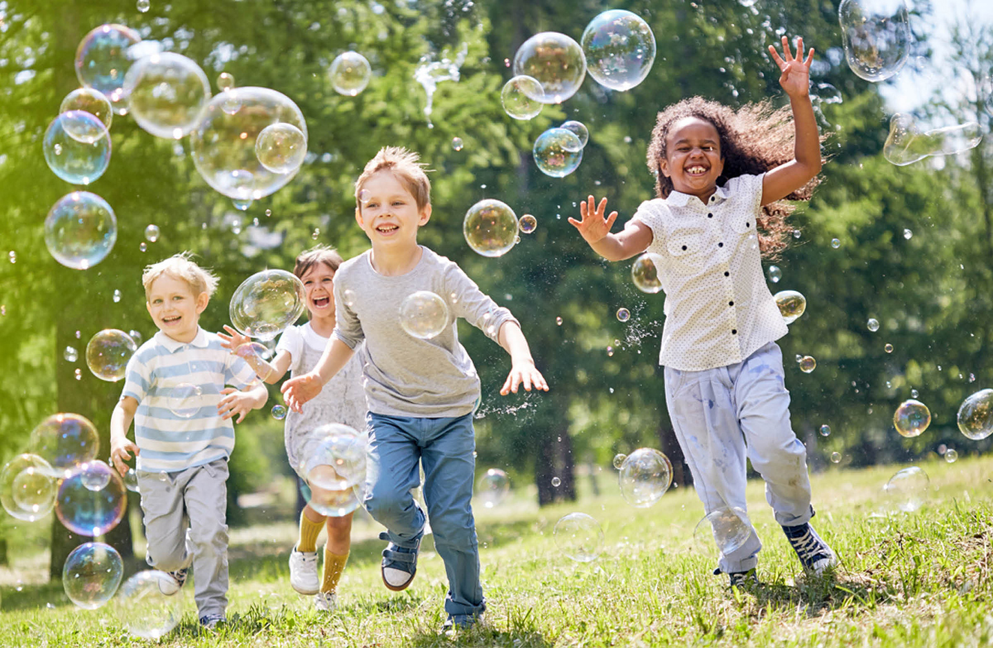 Kinder jagen im Garten Seifenblasen hinterher und haben sichtlich Spaß daran.