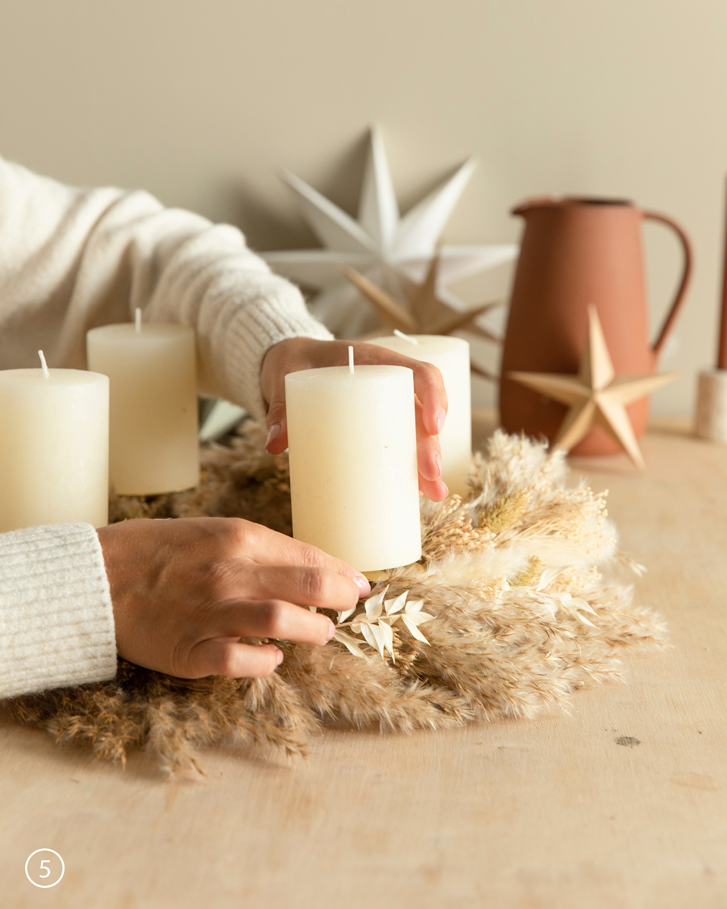 Weiße Kerze wird auf einem Adventskranz aus Trockenblumen befestigt.