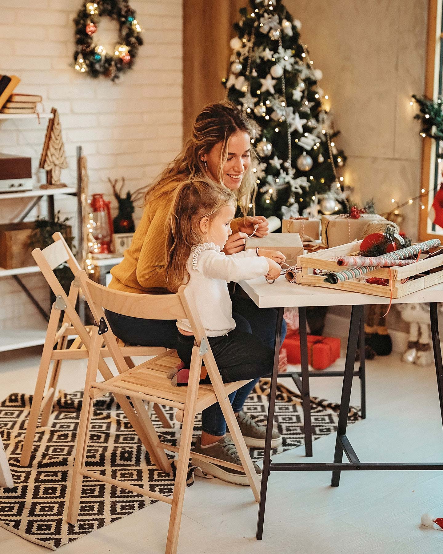 Mama packt am Tisch mit ihrer Tochter Weihnachtsgeschenke ein.