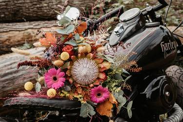 Eine schwarze Harley geschmückt mit einem farbenfrohen Brautstrauß in pink, orange, gelb und rot. 