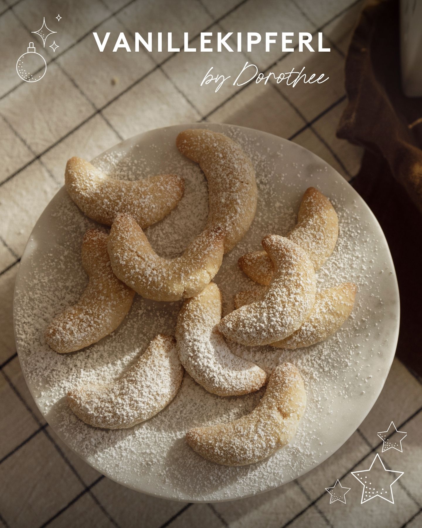 Teller mit puderzuckerbestäubten Vanillekipferl  auf einem Tisch mit karierter Tischdecke